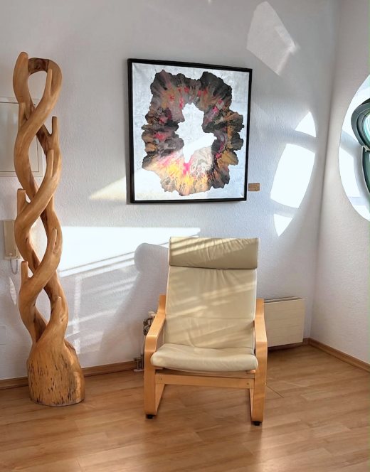 Wartezimmer: Ledersessel neben einer Holzskulptur, darüber ein gerahmtes Bild