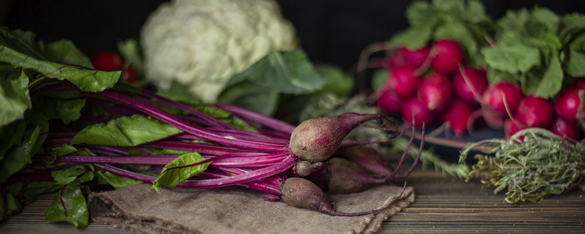 Rote Bete mit Blättern, Radieschen, Blumenkohl und Kräuter auf dunklem Holz