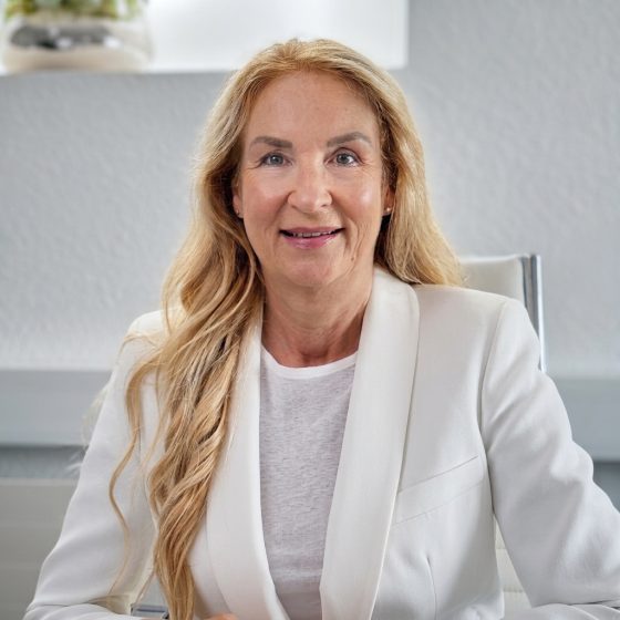 Titelbild Frau Dr. med. Beate Knaur Frau Beate Knaur mit blonden Haaren in einem hellen Anzug, lächelt in einem modernen Büro.